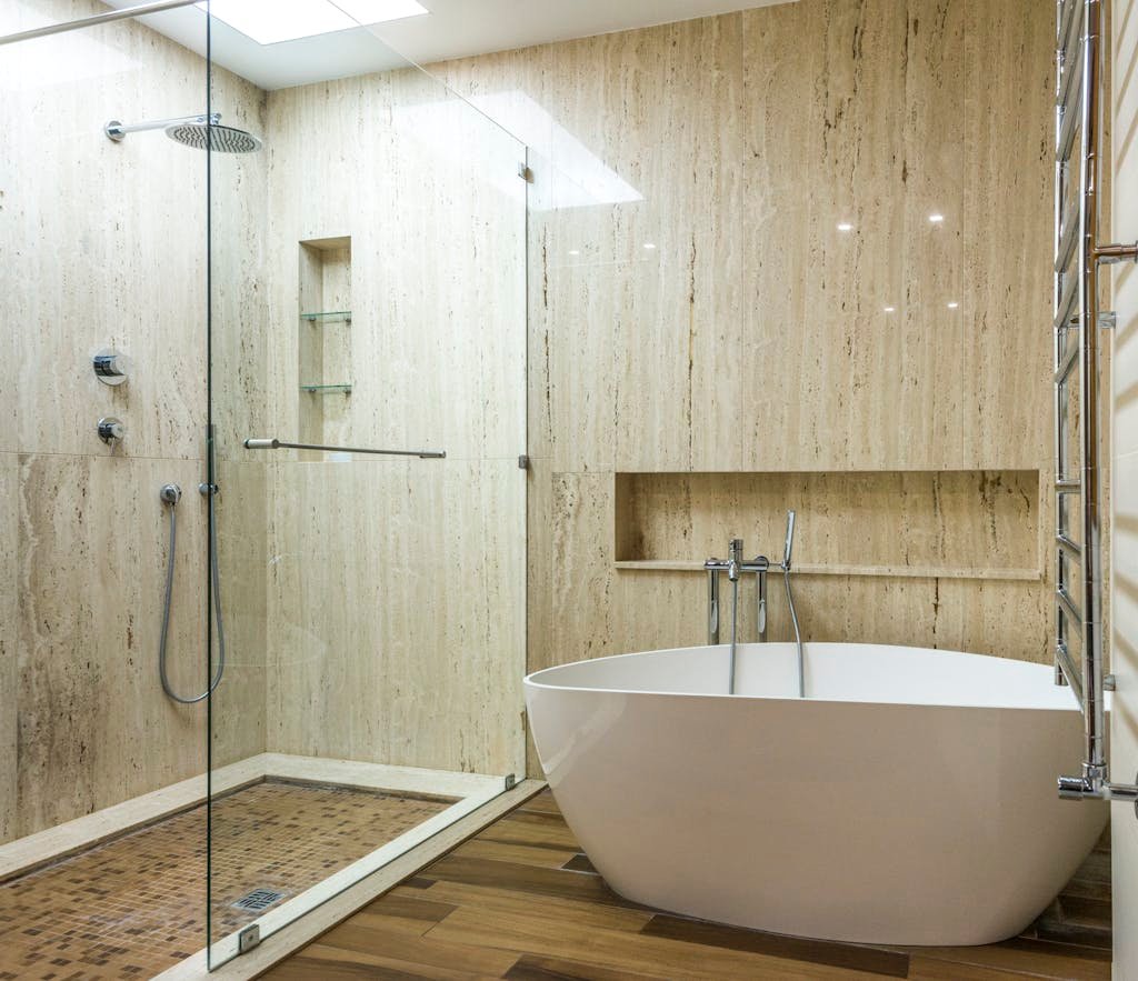 Contemporary bathroom featuring a marble wall, glass shower, and stylish bathtub.