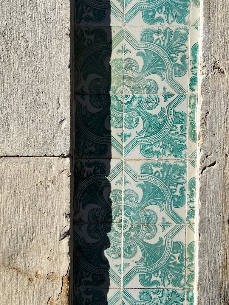 Intricate green tiles cast a shadow on a textured wall, evoking classic architectural charm.