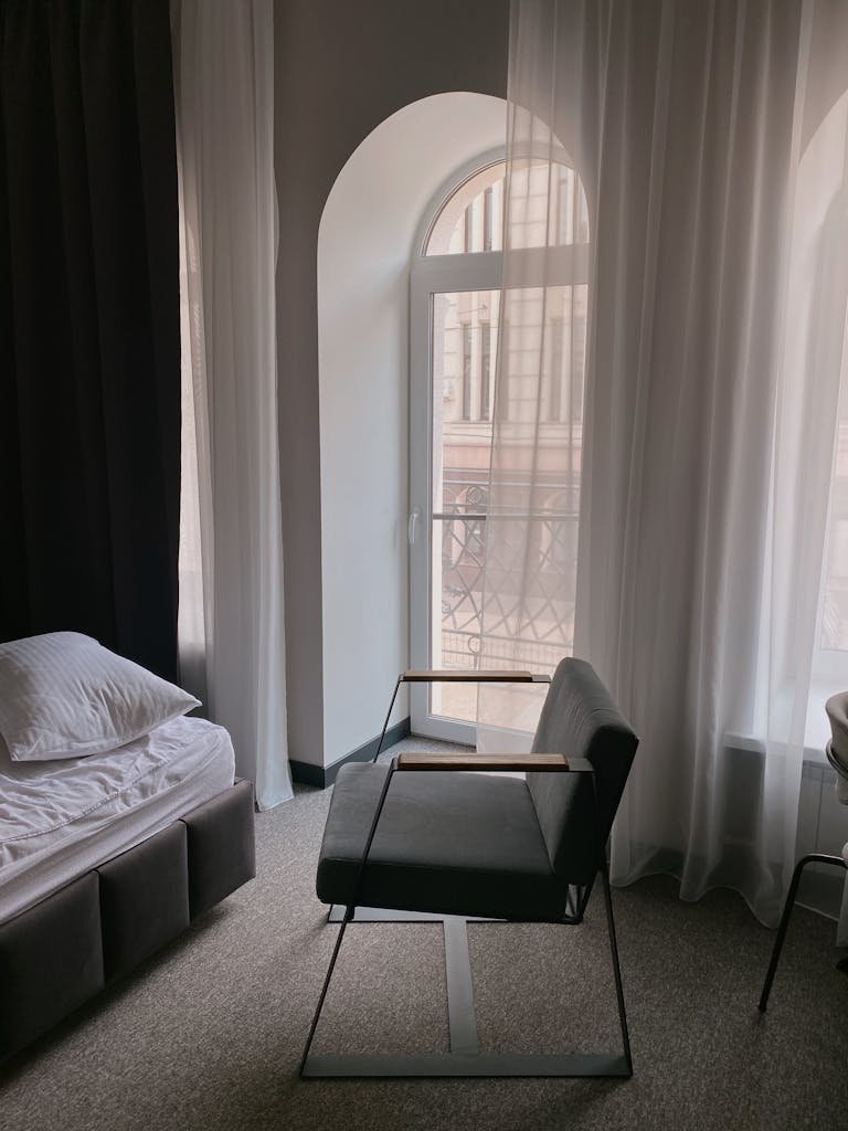 Modern bedroom interior featuring a minimalist design with a grey chair and sheer curtains.